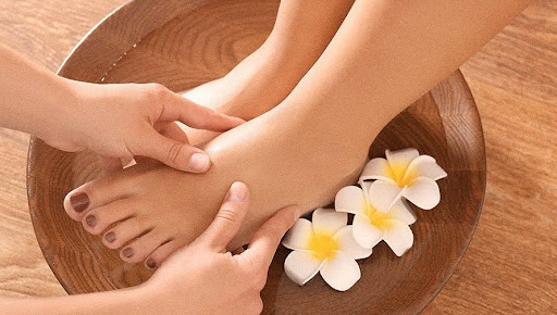 Close-up of a professional massage session in a dimly lit, serene spa environment. Warm, amber lighting highlights the smooth textures of massage oils and the calm expression of a guest. The background is softly blurred, showing hints of dark wood and stone elements. The mood is deeply relaxing and intimate, emphasizing a digital detox and physical restoration.